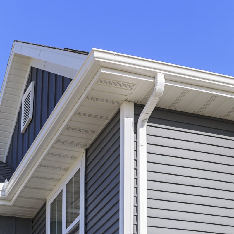 New home with white gutters, soffit and grey vinyl siding. Blue sky is in the background